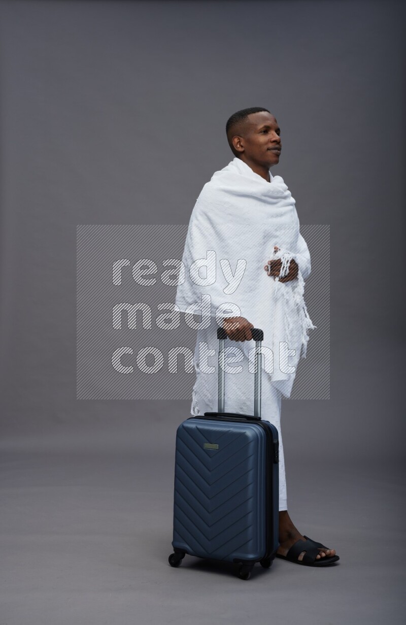 A man wearing Ehram Standing holding traveling bag on gray background