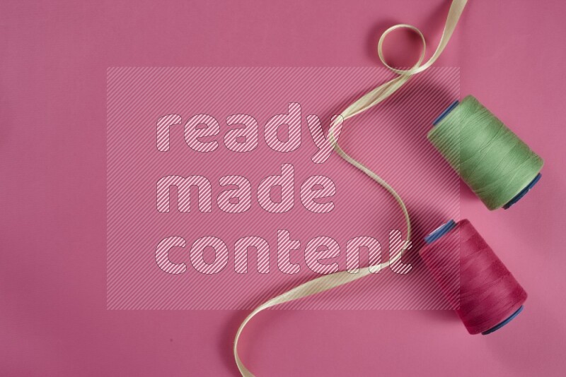 A green and pink collection of sewing and tailoring tools arranged on a pink background