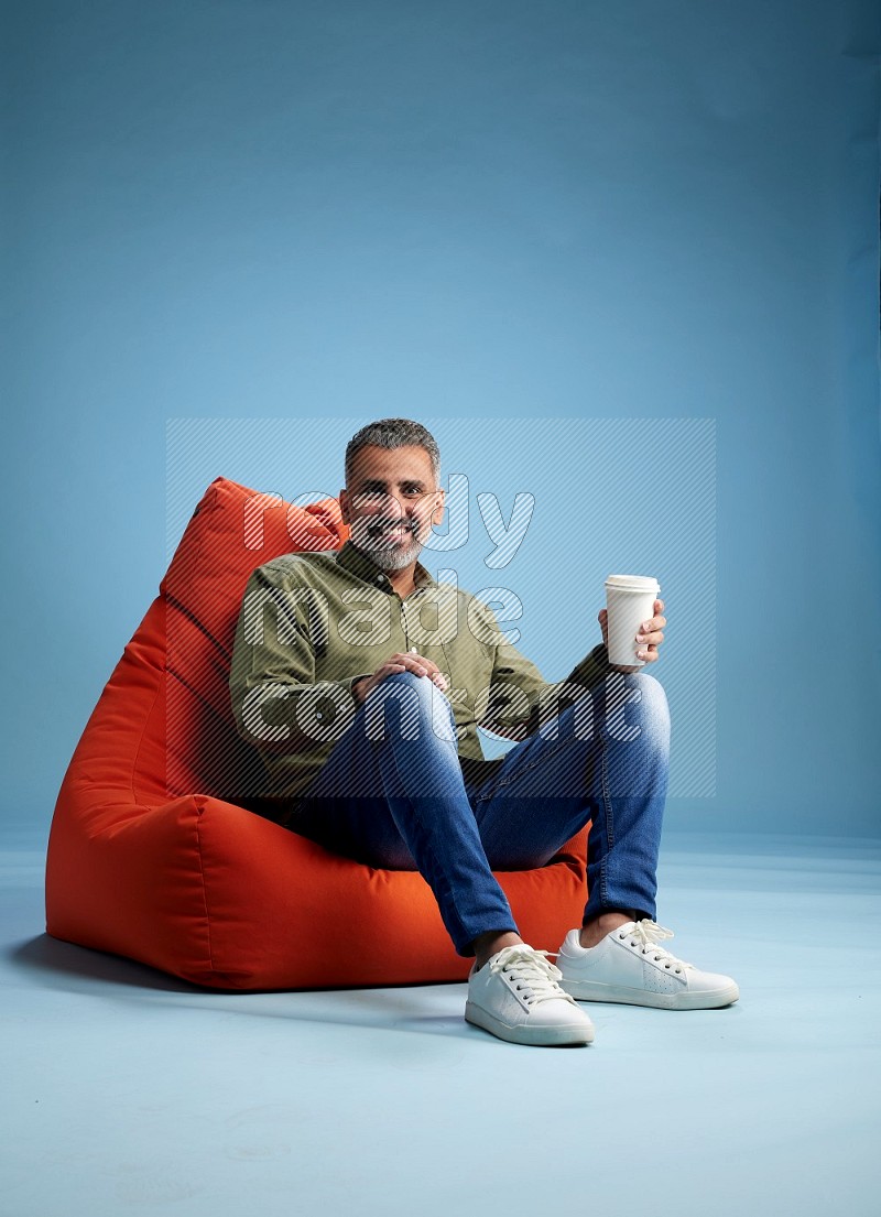 A man sitting on an orange beanbag and drinking coffee