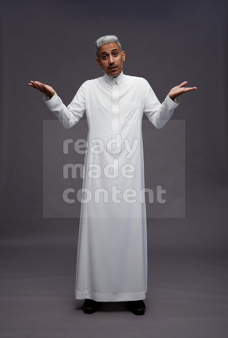 Saudi man wearing thob standing interacting with the camera on gray background