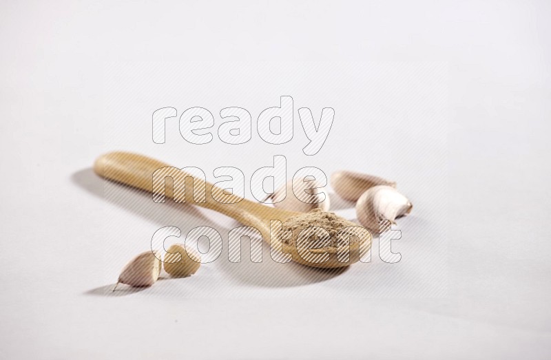 A wooden spoon full of garlic powder and garlic cloves beside it on a white flooring in different angles