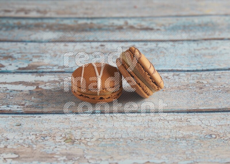 45º Shot of of two assorted Brown Irish Cream, and light brown Almond Cream macarons next to each other on light blue background