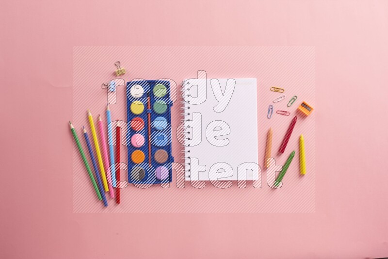 A blank open notebook with coloring pens on rose background