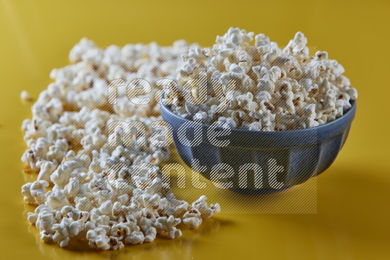 A blue pottery bowl full of popcorn with popcorn beside it on a yellow background in different angles