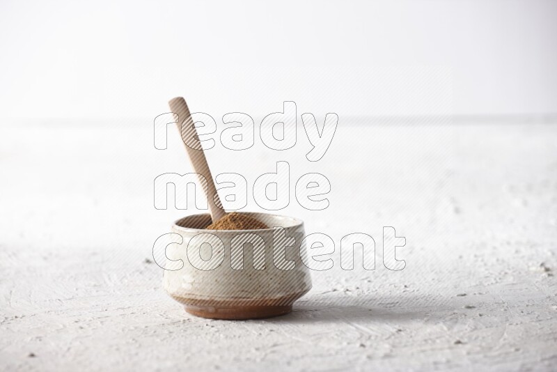 Ceramic beige bowl full of cinnamon powder with a wooden spoon on a textured white background