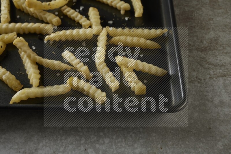 crinkle fries in a black stainless steel rectangle tray on grey textured counter top