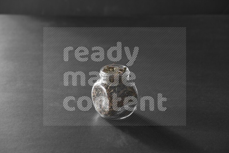 A glass spice jar full of basil on black flooring