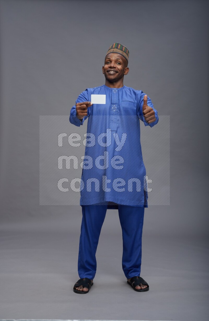 Man wearing Nigerian outfit standing holding ATM card on gray background