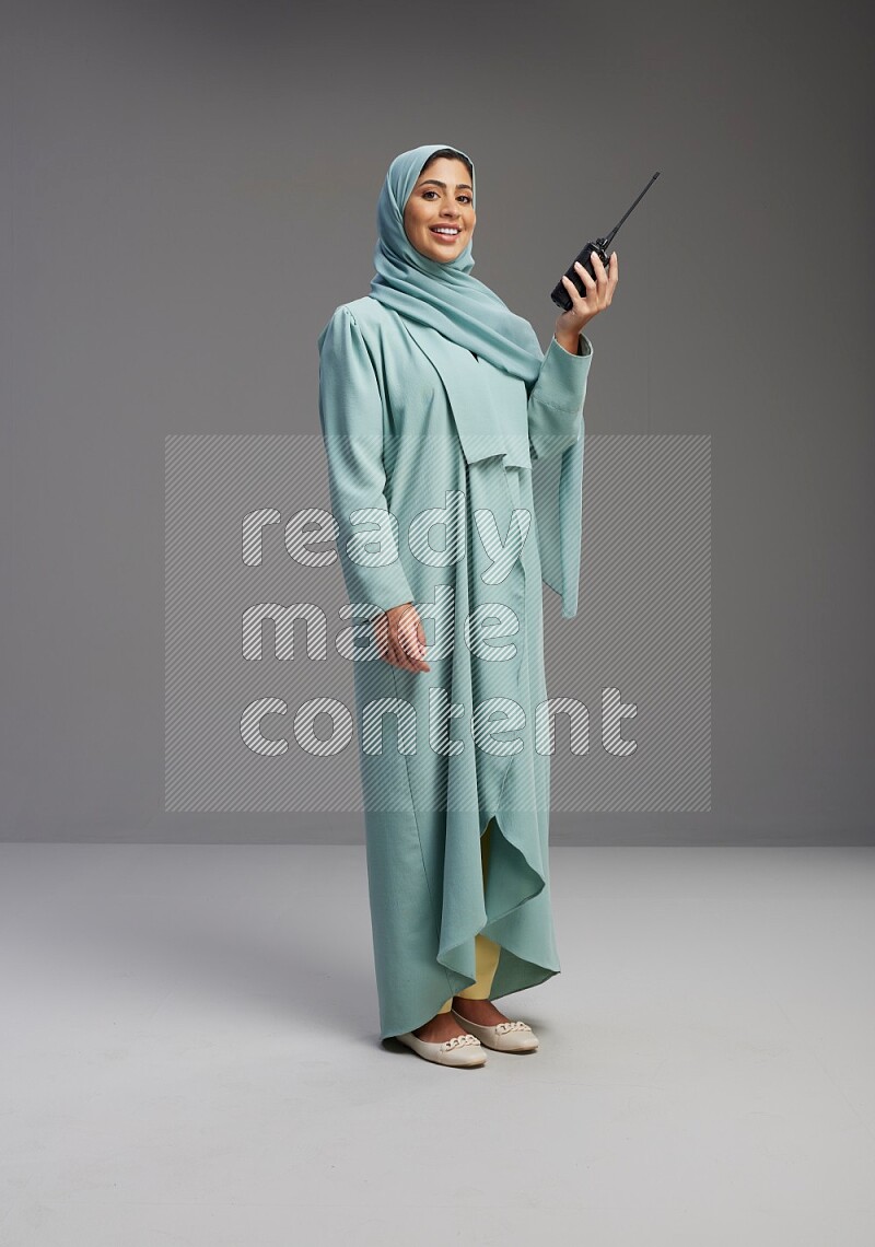 Saudi Woman wearing Abaya standing holding walkie-talkie on Gray background