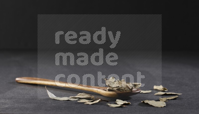 ملعقة خشبية كبيرة ممتلئة بأوراق الغار المجففة علي خلفية سوداء