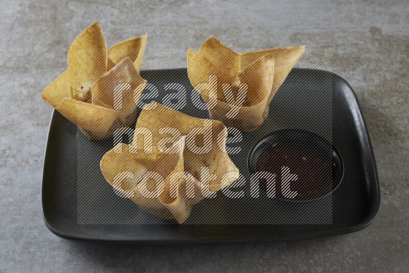 wonton cups with soy sauce ramkin on rectangle dark grey ceramic plate on grey textured counter top