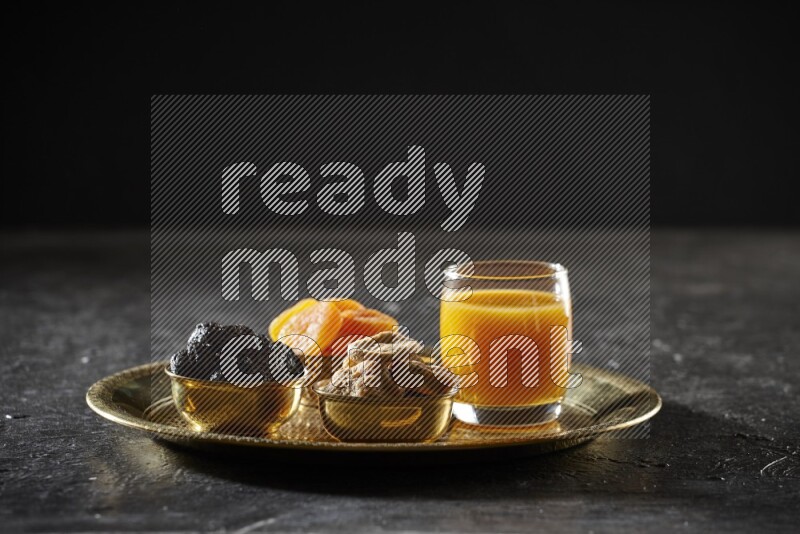 Dried fruits in metal bowls with qamar eldin on a tray in dark setup