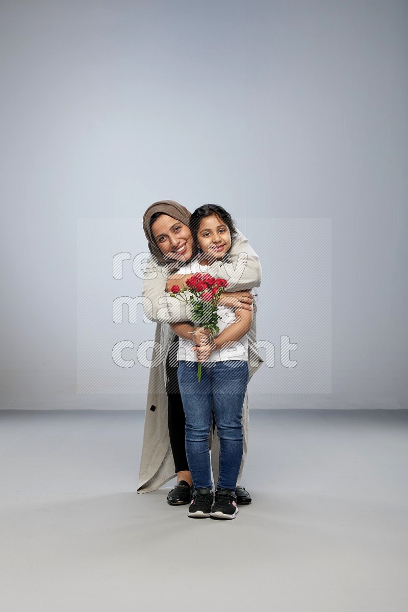 A girl standing giving flowers to her mother on gray background