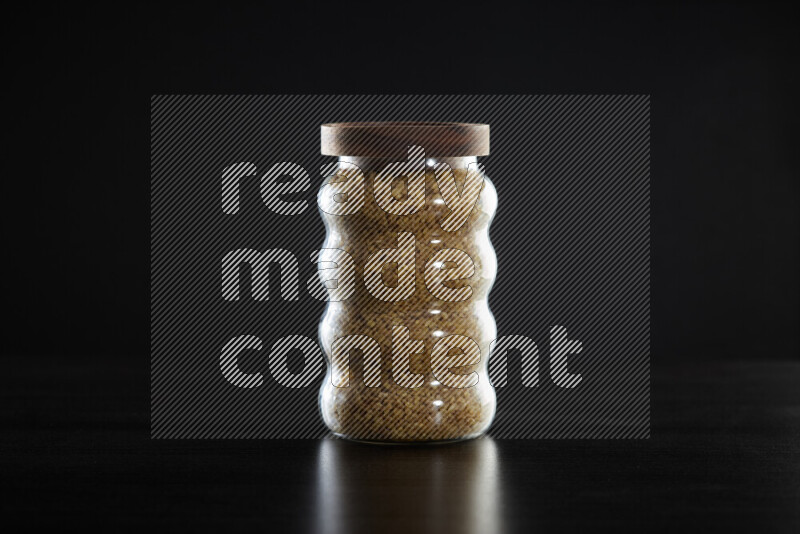 Coarse bulgur in a glass jar on black background