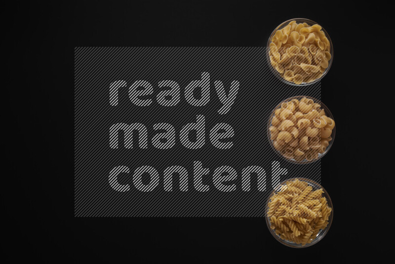 Different pasta types in 3 glass bowls on black background