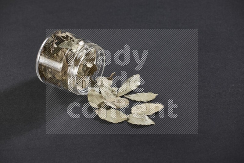 وعاء زجاجي ممتلئ بأوراق الغار والوعاء مقلوب وبعض الأوراق متناثرة خارجه علي خلفية سوداء