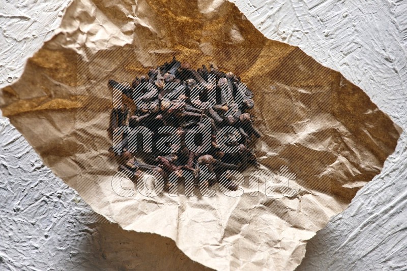 Cloves on crumpled piece of paper on a textured white flooring