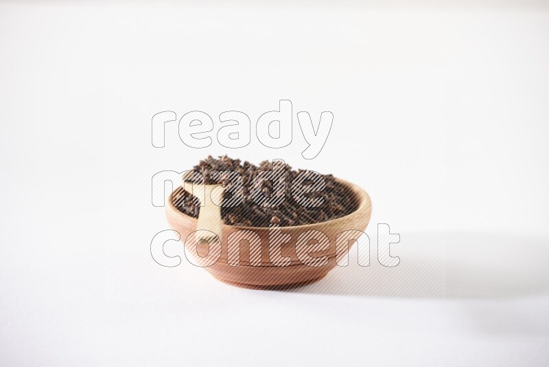 A wooden bowl and a wooden spoon full of cloves on a white flooring