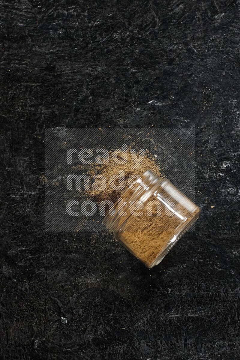 وعاء زجاجي مقلوب ممتلئ ببودرة الكمون والبودرة تناثرت منه على خلفية سوداء
