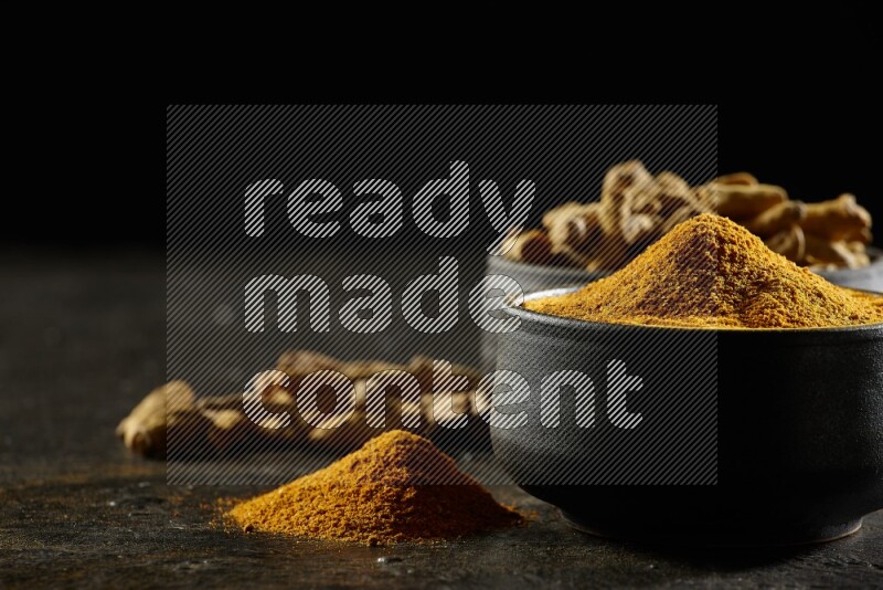 وعاءان من الفخار باللون الأسود، أحدهما ممتلئ ببودرة الكركم والآخر ممتلئ بأصابع كاملة من الكركم المجفف على خلفية سوداء