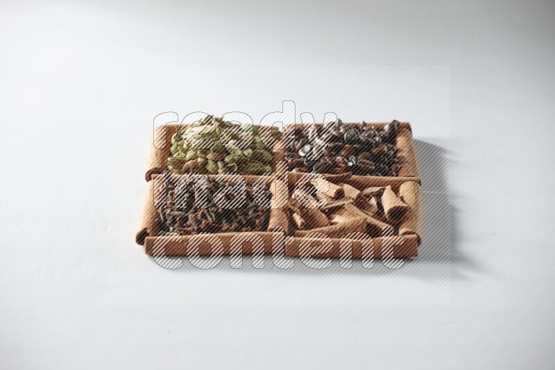 4 مربعات من أعواد القرفة ممتلئة بحبوب القهوة والقرفة والقرنفل والهيل على أرضية بيضاء