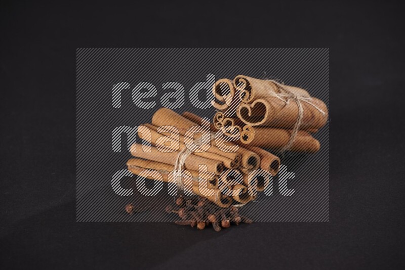 Two bounded stacks of cinnamon sticks with cloves on black background