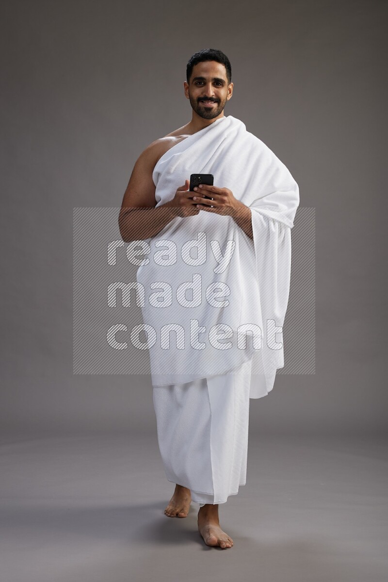 A man wearing Ehram Standing texting on phone on gray background