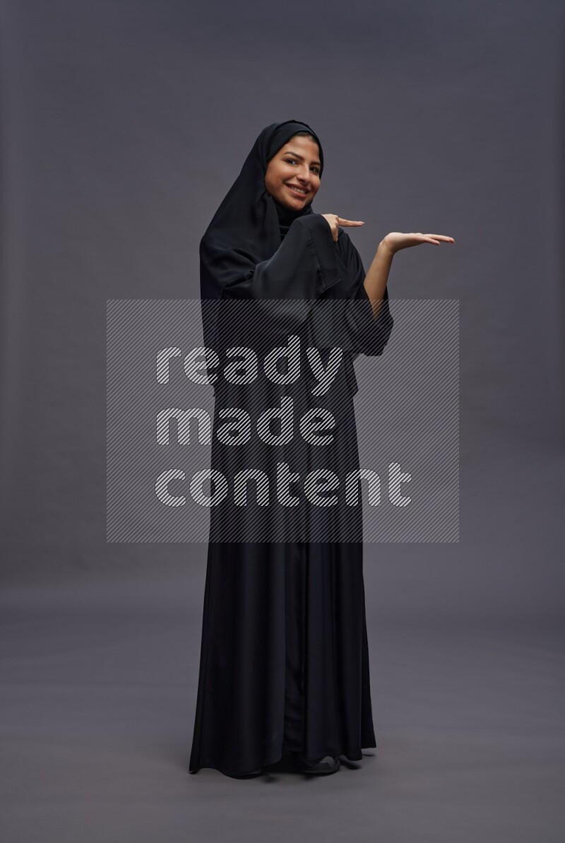 Saudi woman wearing Abaya standing interacting with the camera on gray background