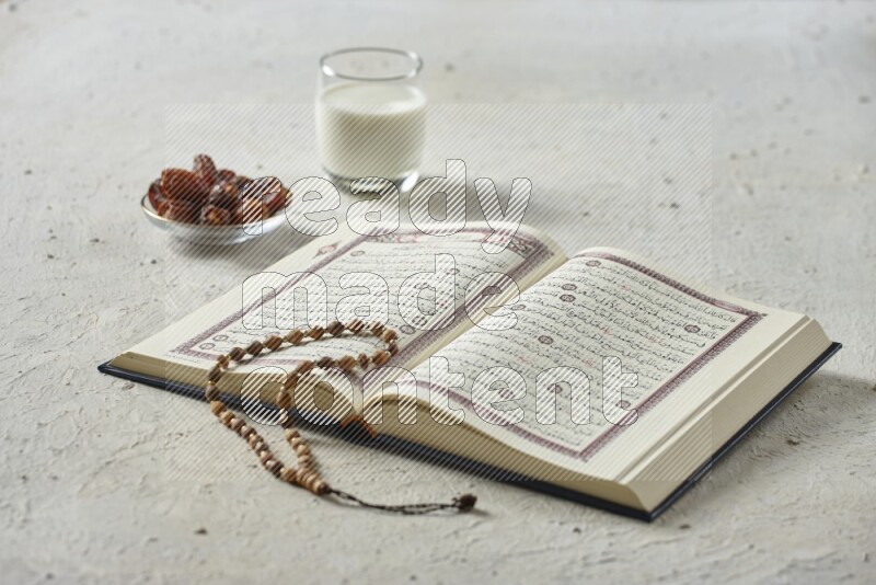 Quran with dates, prayer beads and different drinks all placed on textured white background