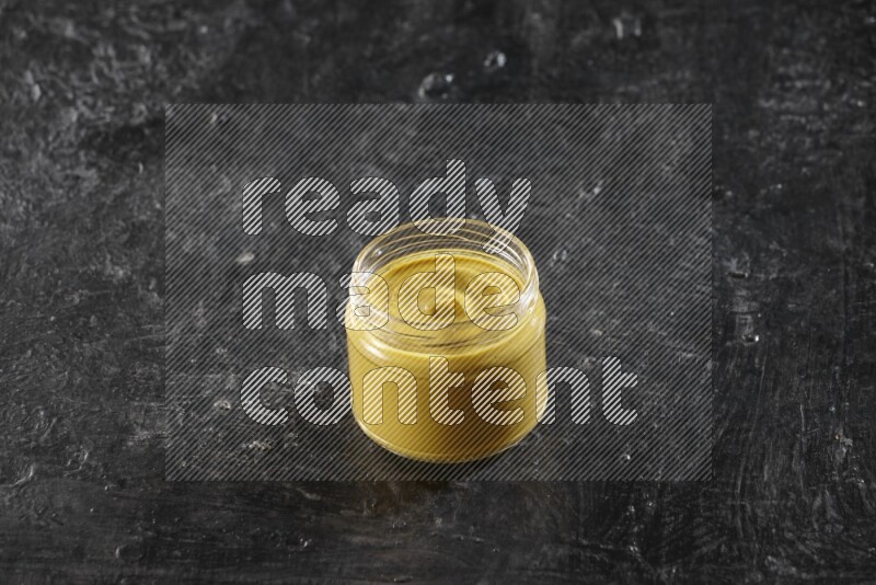 A glass jar full of mustard paste on a textured black flooring