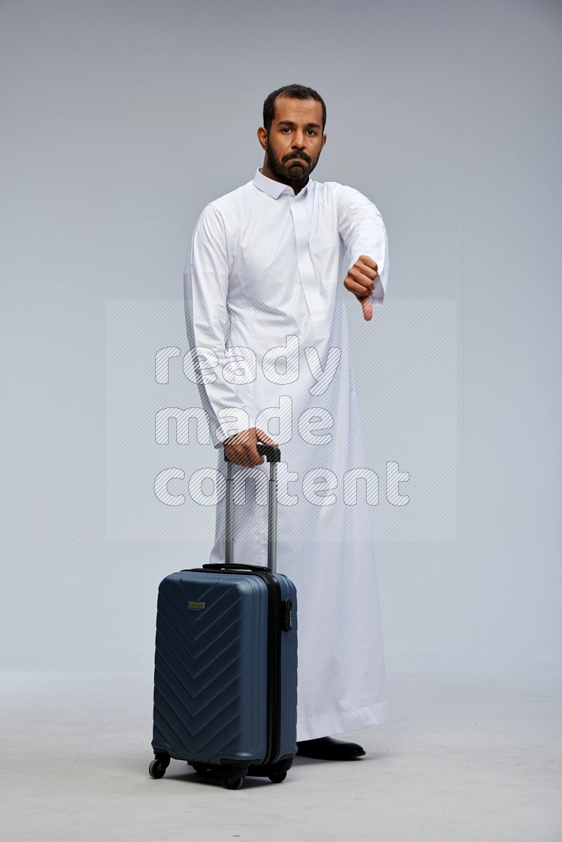 Saudi man wearing thob standing holding Travel bag on Gray background