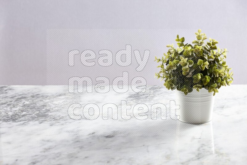 Green artificial plant in white pot on light grey marble background