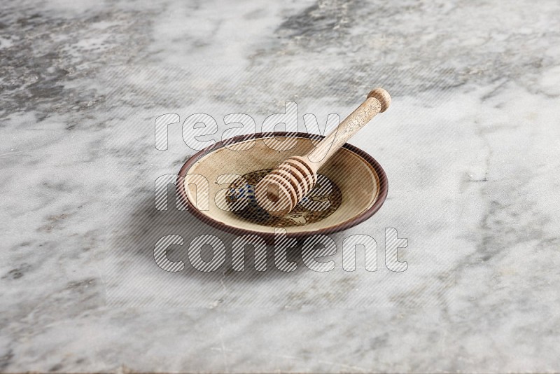 Decorative Pottery Plate with wooden honey handle in it, on grey marble flooring, 45 degree angle