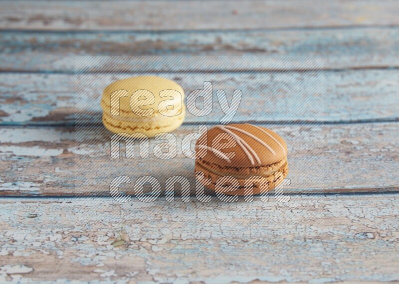 45º Shot of of two assorted Brown Irish Cream, and Yellow Vanilla macarons on light blue background
