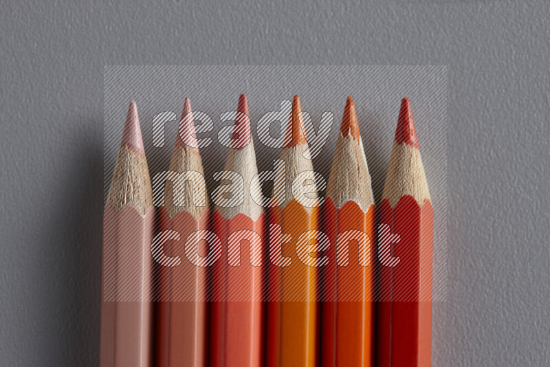 A collection of colored pencils arranged showcasing a gradient of orange hues on grey background