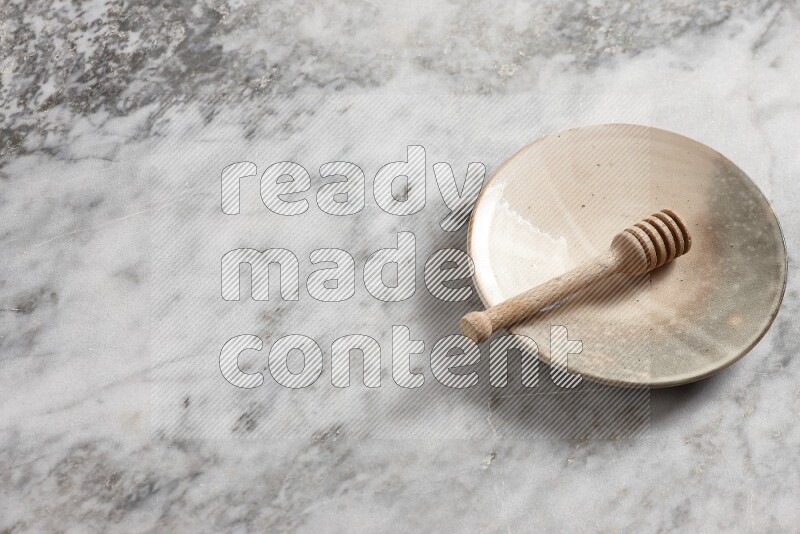 Multicolored pottery plate with wooden honey dipper in it on grey marble background