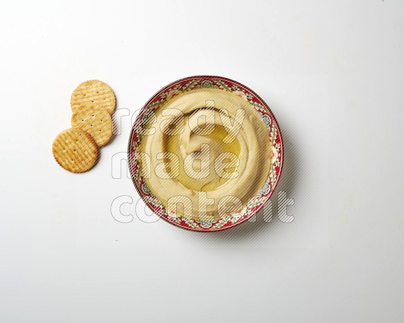 Hummus in a red plate with patterns garnished with olive oil on a white background