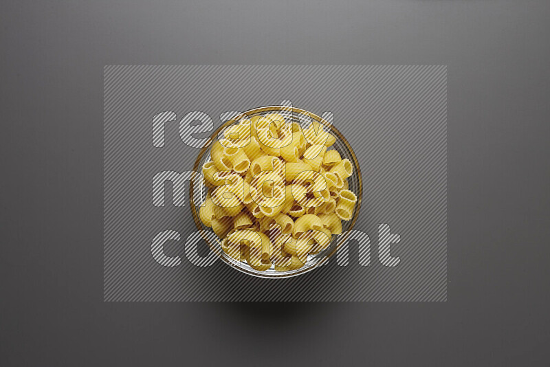 Elbow pasta in a glass bowl on grey background