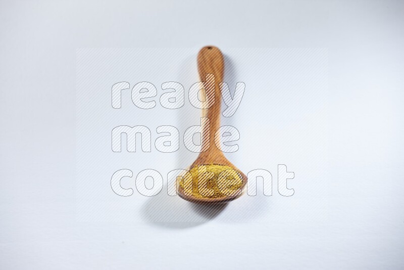 A wooden ladle full of turmeric powder on white flooring