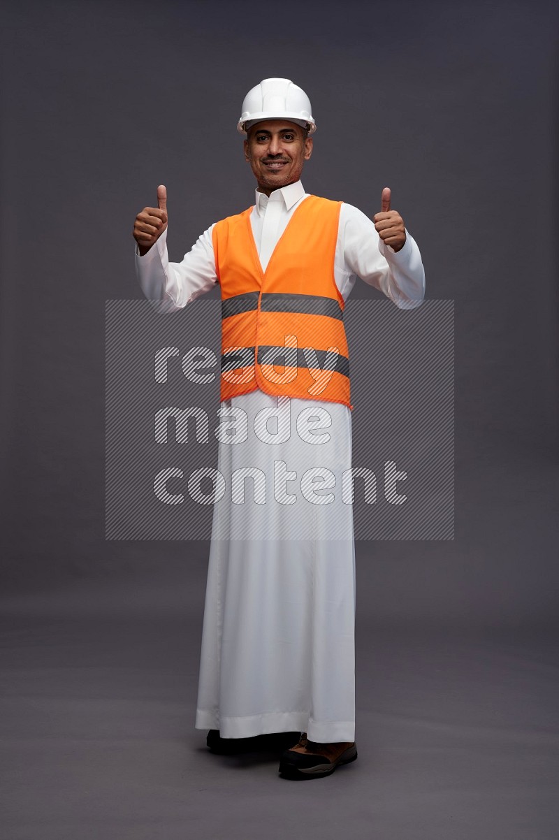 Saudi man wearing thob with engineer vest standing interacting with the camera on gray background