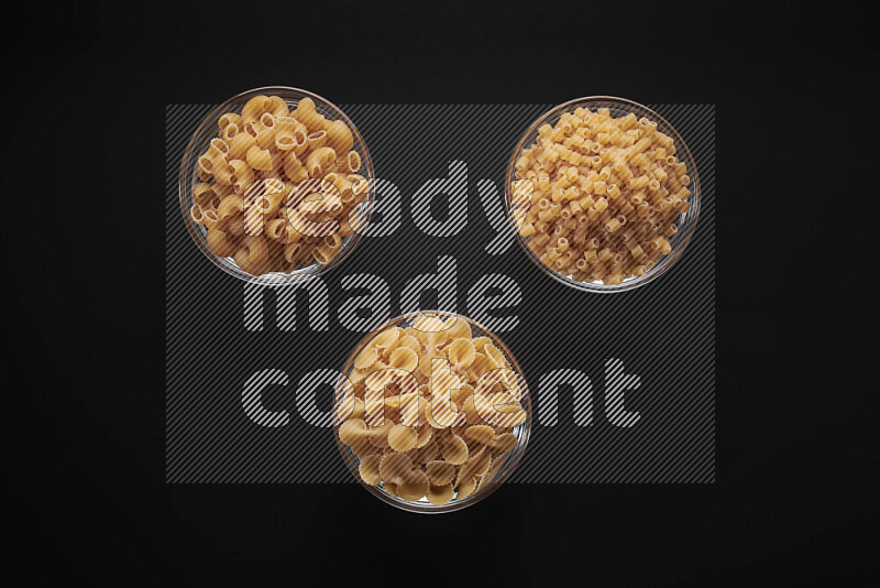 Different pasta types in glass bowls on black background