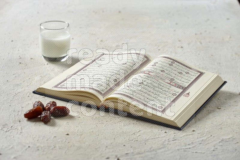 Quran with dates, prayer beads and different drinks all placed on textured white background