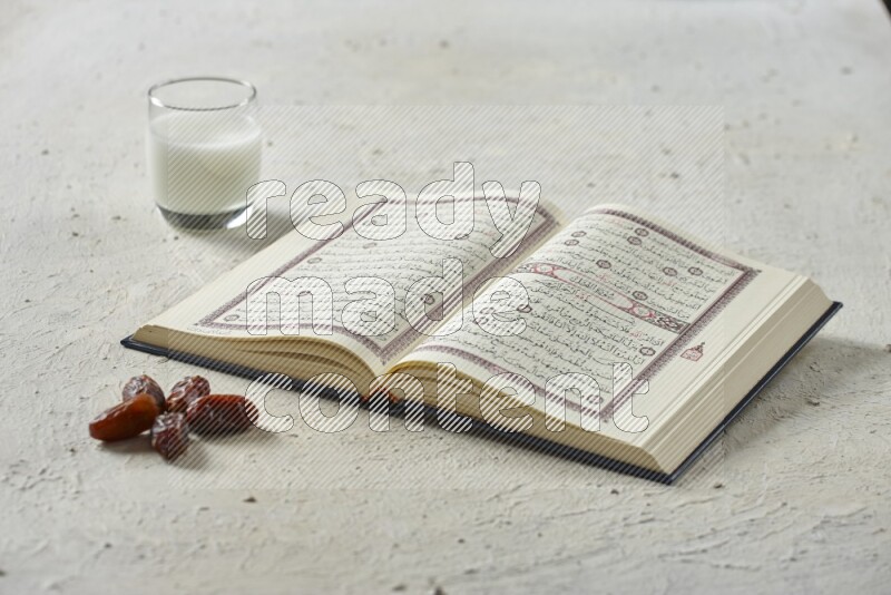 Quran with dates, prayer beads and different drinks all placed on textured white background