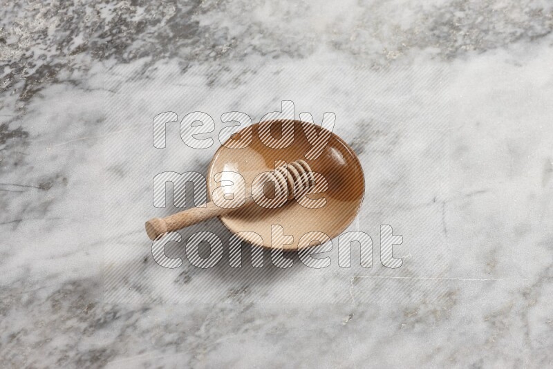 Multicolored pottery plate with wooden honey dipper in it on grey marble background