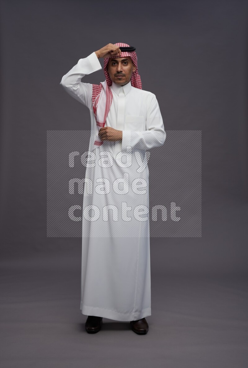 Saudi man wearing thob and shomag standing hands behind head on gray background