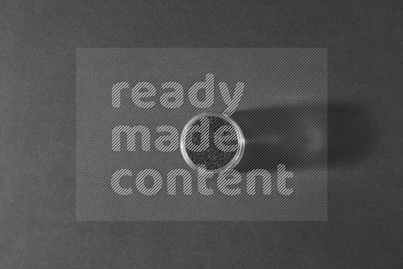 وعاء زجاجي ممتلئ ببذور حبة البركة علي خلفية سوداء