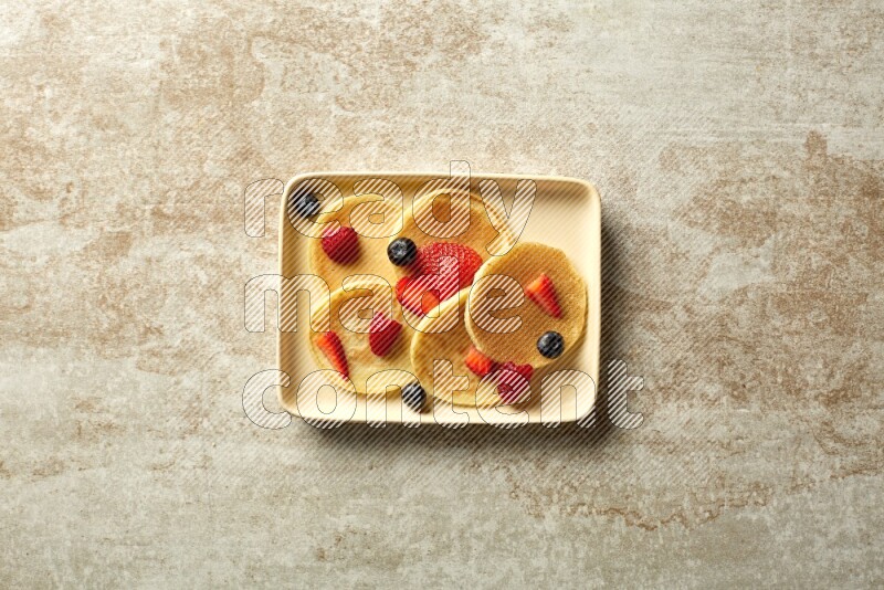 Five stacked mixed berries mini pancakes in a rectangular plate on beige background