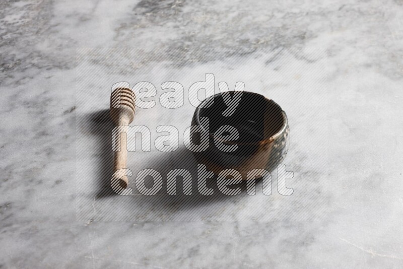 Multicolored pottery bowl with wooden honey dipper on the side on grey marble background