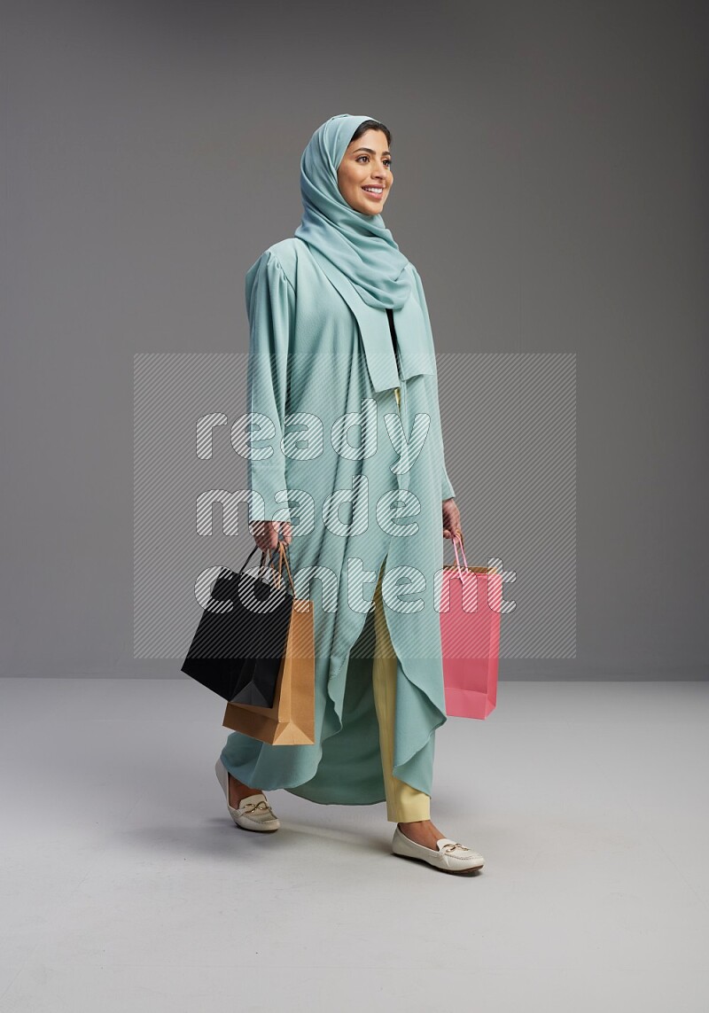 Saudi Woman wearing Abaya standing holding shopping bag on Gray background