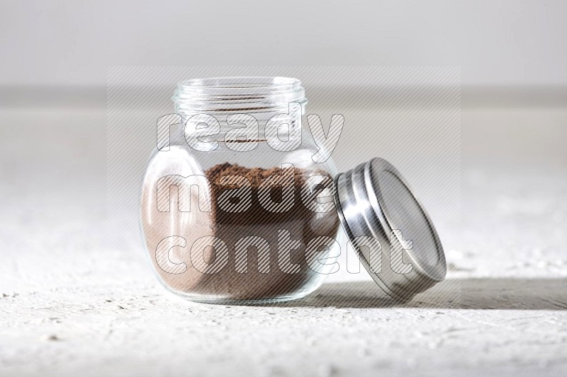 A glass spice jar full of cloves powder on textured white flooring